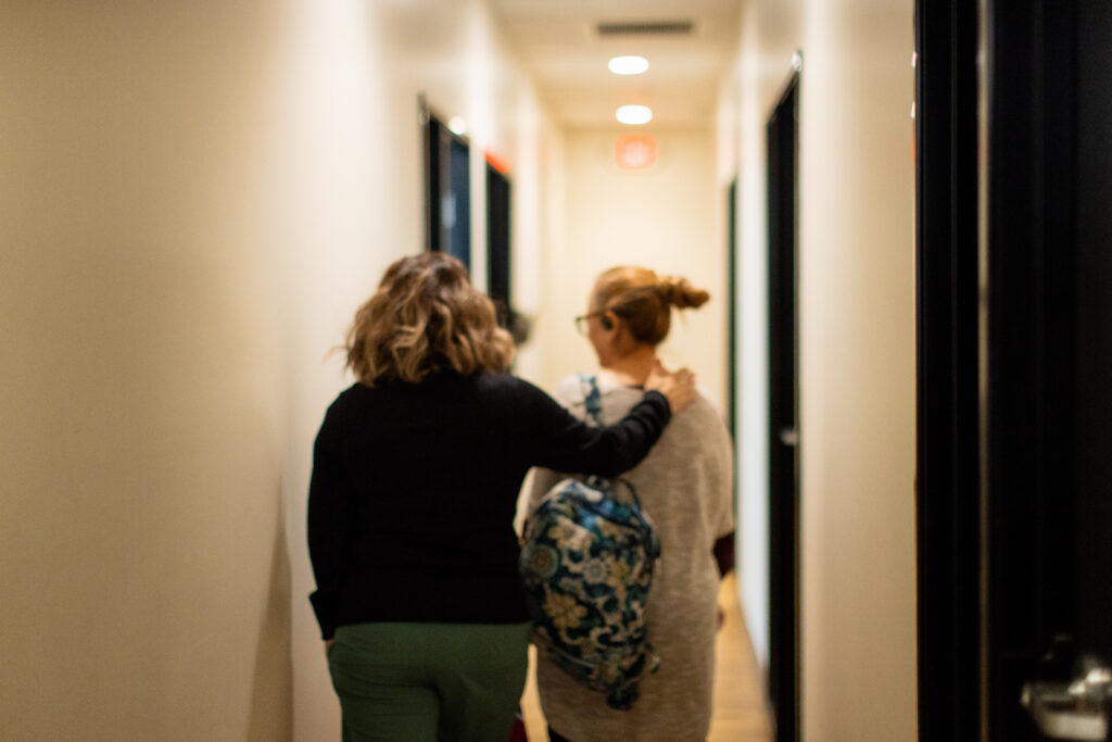 A Hope Women’s Center staff member walks alongside a woman down a hallway, gently placing a hand on her shoulder in a gesture of care and support.