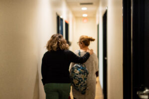A Hope Women’s Center staff member walks alongside a woman down a hallway, gently placing a hand on her shoulder in a gesture of care and support.
